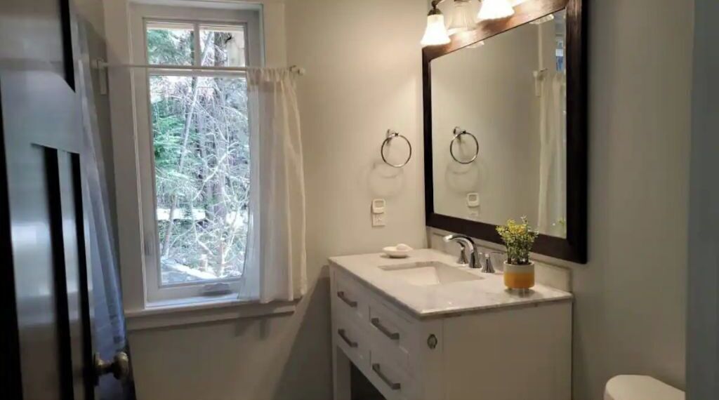 Une salle de bain avec une fenêtre, un lavabo, un miroir et des toilettes.