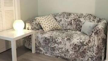 Una habitación con un sofá estampado de flores, una mesita blanca con una lámpara y una alfombra con diseño.