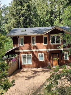 Situated in a forested area, this cabin features a front porch with a railing and potted plants.