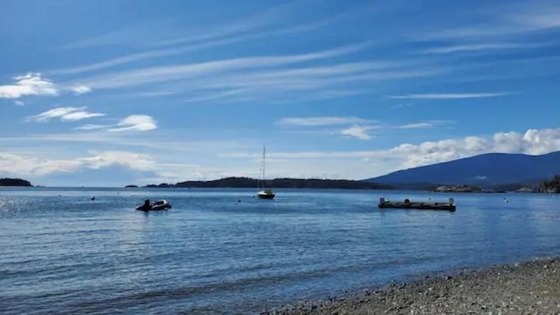 Un lago tranquilo con barcos, una orilla rocosa y montañas distantes bajo un cielo despejado.