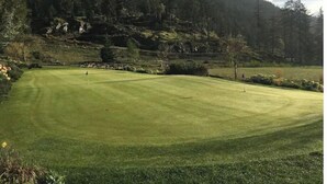 Un campo de golf con un césped cuidado, rodeado de bosque denso y terreno rocoso.