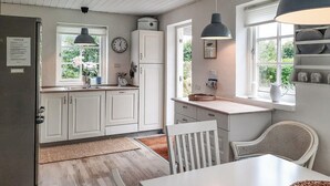 A kitchen with white cabinets, a sink, a clock, and a window with a view of greenery.