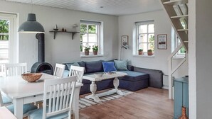 A cozy living room with a sofa, a dining table with chairs, a fireplace, and a staircase.