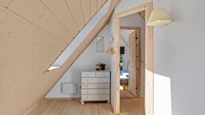 A loft bedroom with a sloped ceiling, a dresser, a mirror, and a hanging light fixture.