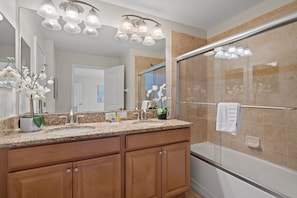 A bathroom with a granite countertop, a double sink, a large mirror, and a glass shower enclosure.