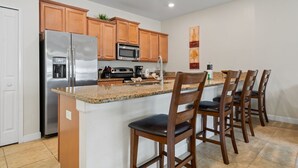 Una cocina con armarios de madera, un refrigerador de acero inoxidable, un microondas, un fregadero y taburetes de bar.