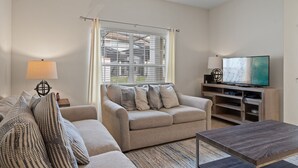 Una sala de estar con sofá, mesa de centro, televisor y ventana con persianas.