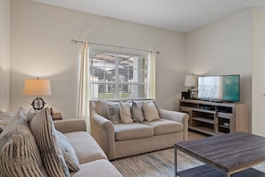 A living room with a sofa, a coffee table, a TV, and a window with blinds.