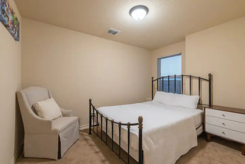 A bedroom with a bed, a chair, a dresser, and a window.