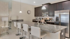 A modern kitchen with granite countertops, stainless steel appliances, and white bar stools.