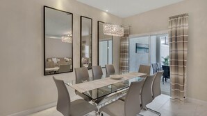 A modern dining area with a glass table, grey upholstered chairs, and a chandelier.