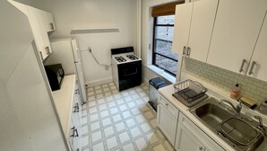 Cocina compacta con armarios blancos, cocina a gas, lavamanos y ventana con vistas.