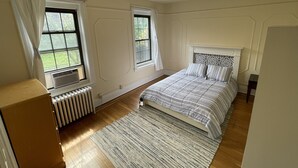 Un dormitorio con una cama, dos ventanas, un radiador y una lámpara en el techo.