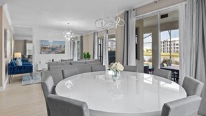 Ein modernes Wohnzimmer mit einem runden Esstisch, grauen Sofas und einem großen Fenster mit Vorhängen.