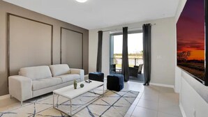 Uma sala de estar moderna com um sofá branco, uma mesa de centro e uma janela grande com cortinas.