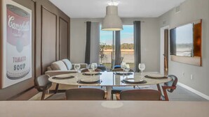 Uma sala de jantar com uma mesa posta para seis pessoas, um sofá e uma janela grande com cortinas.