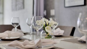 Een eettafel met witte servetten, glanzende wijnglazen en een vaas met witte bloemen.