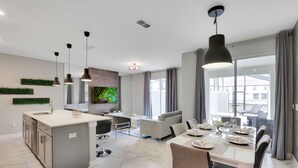 Een moderne keuken met een centraal eiland, een eethoek met een tafel voor vier personen, en een zithoek met een bank en stoelen.