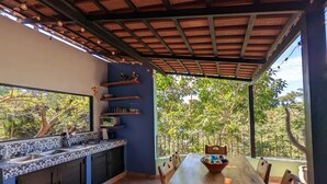 A kitchen with a large island, a dining table, and chairs. There is a window with a view of trees. - Digital Nomad's Dream in Paradise II (Sayulita)