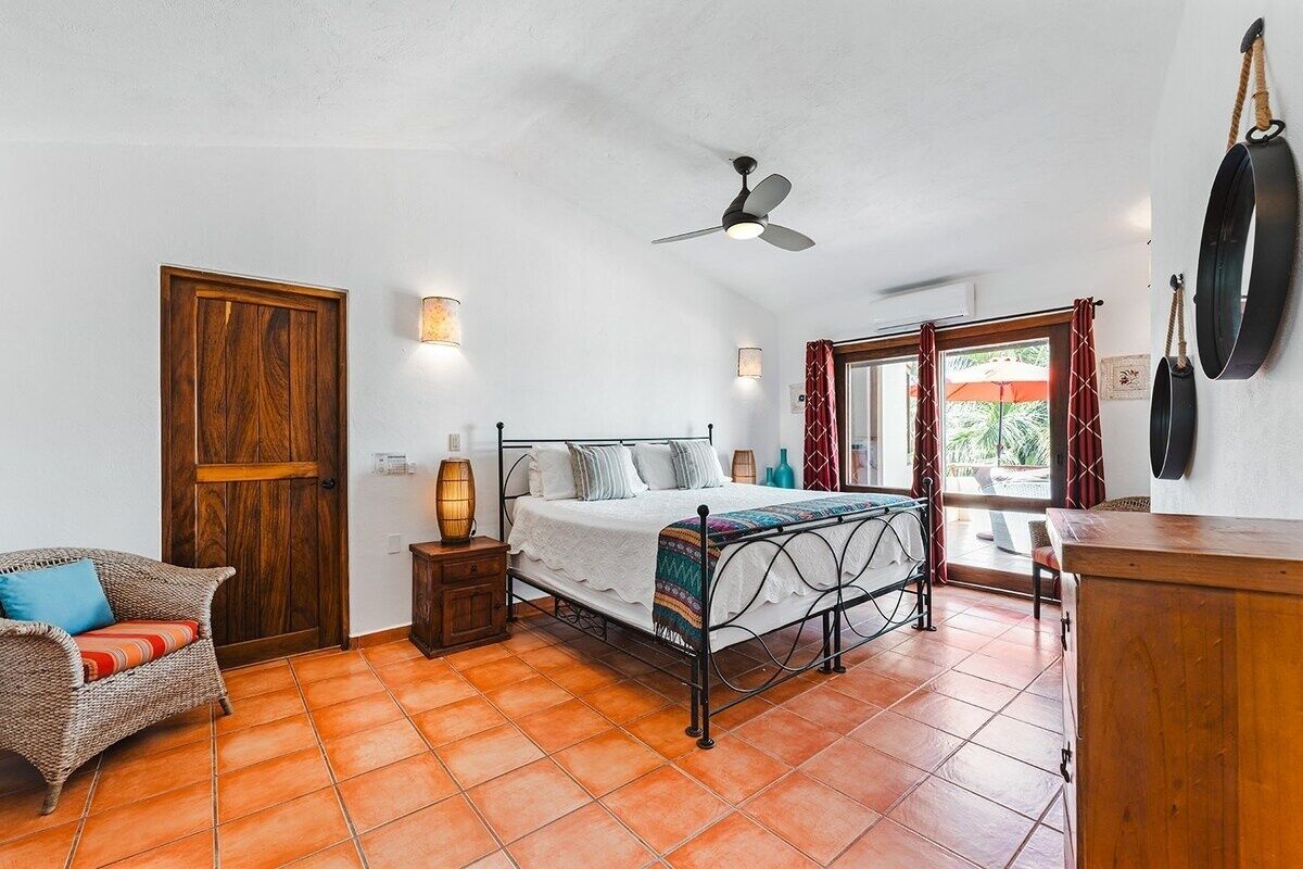 Een slaapkamer met een bed, een stoel, een nachtkastje, een plafondventilator en een raam met gordijnen.