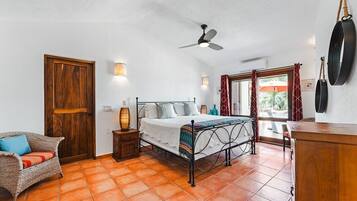 Een slaapkamer met een bed, een stoel, een nachtkastje, een plafondventilator en een raam met gordijnen.