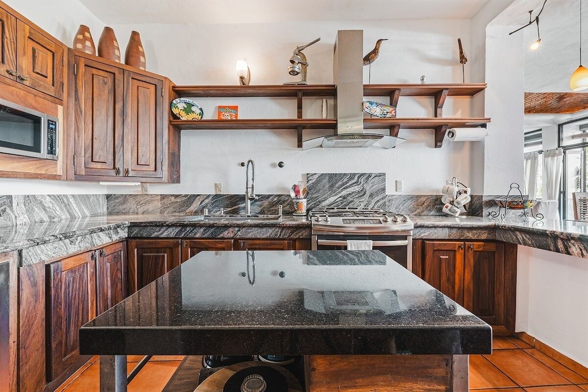 A kitchen with dark wooden cabinets, a black marble countertop, and a central island.