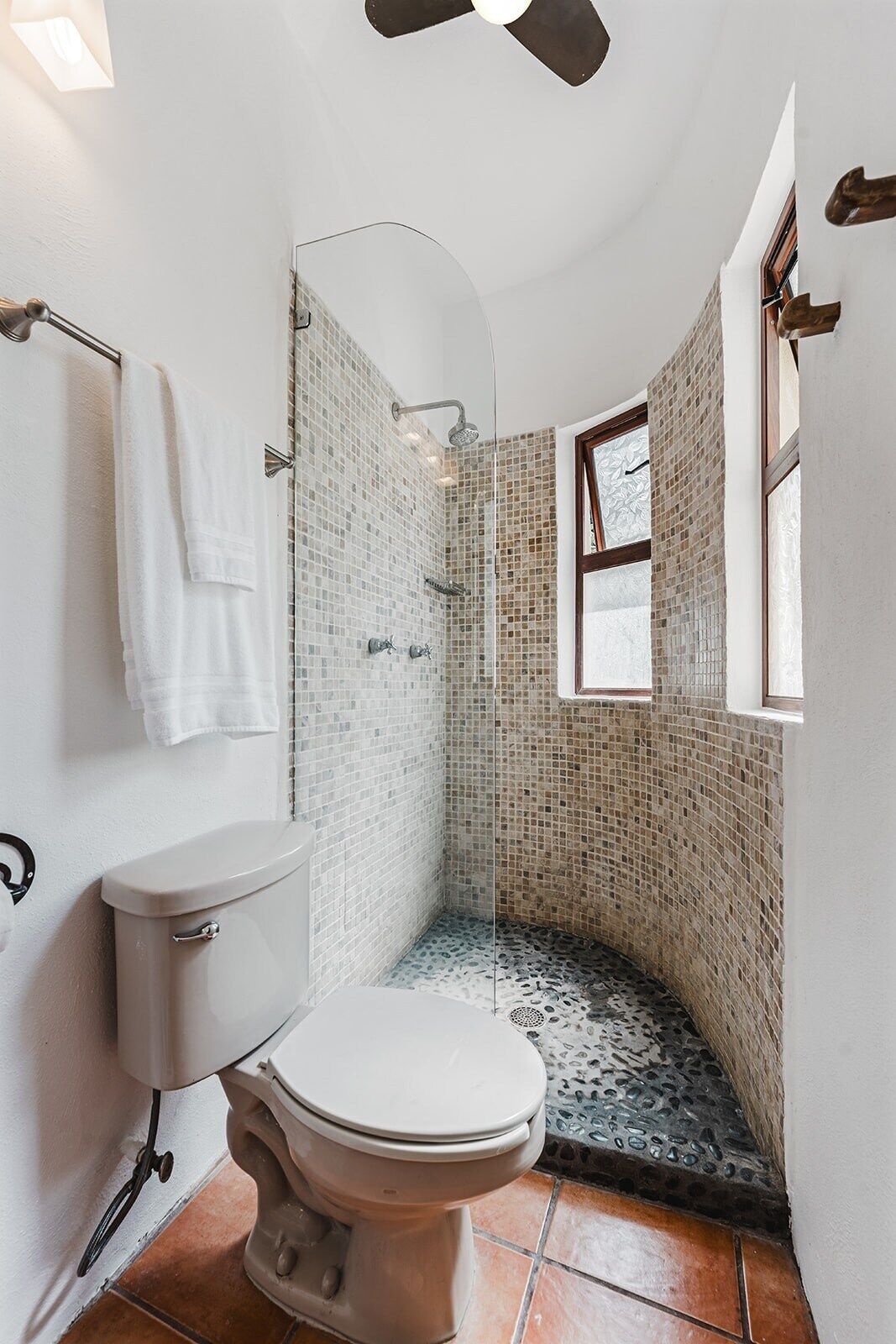 A compact bathroom with a toilet, shower, and a small window.