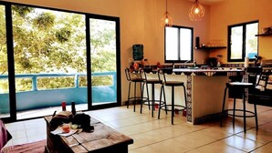 A spacious living area with a large window, a kitchen with bar stools, and a dining table.