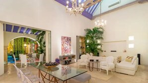 Amplia sala de estar con una mesa de comedor de vidrio, sofás blancos y un candelabro.