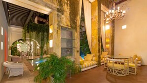 Un espacio interior acogedor con piso de madera, una piscina y una zona de estar con cojines amarillos.