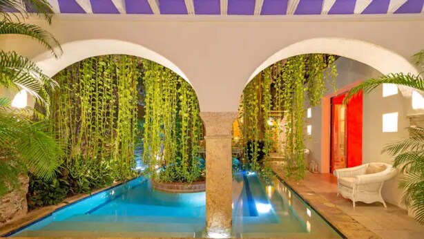 Un área de piscina interior con una columna central, arcos y abundante vegetación.