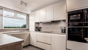 A modern kitchen with a large window, built-in appliances, and a minimalist design. - West Sands - Donnini Apartments (Ayr)