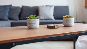 A modern living room with a wooden coffee table, two potted plants, and a grey sofa with cushions. - West Sands - Donnini Apartments (Ayr)