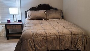 Un dormitorio con cama, mesita de noche, lámpara y ventana con persianas.