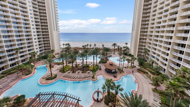 A resort with a central swimming pool surrounded by palm trees and a beach view. - Shores of Panama 814~ 2 Bdrm (Panama City Beach)