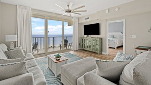 A spacious living room with a large sofa, a television, and a balcony with a view of the sea. - Shores of Panama 814~ 2 Bdrm (Panama City Beach)