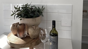 Une cuisine avec une horloge murale, une plante en pot, une bouteille de vin et une planche à découper en bois.