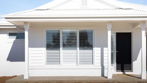 Une maison blanche avec un toit à pignon, un porche à l’avant et une porte noire.