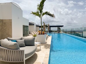 A modern outdoor pool area with a sofa, lounge chairs, and a palm tree. - SERENADA 2nd floor 2 bedroom condo By DPM (Playa del Carmen)