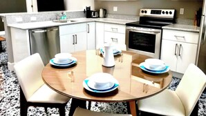A modern kitchen with white cabinets, stainless steel appliances, and a round dining table set for four. - Petaluma Warehouse Loft Collection (Petaluma)