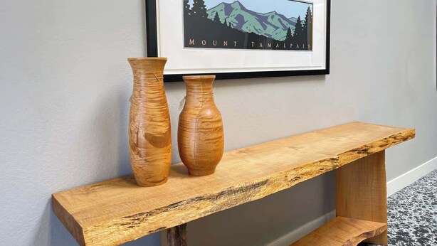 A wooden console table with two wooden vases on it, placed against a wall with a framed picture above. - Petaluma Warehouse Loft Collection (Petaluma)