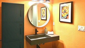 A bathroom with a round mirror, a sink, and three overhead lights. There are two framed artworks on the wall. - Petaluma Warehouse Loft Collection (Petaluma)