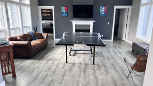 A living room with a ping pong table, a sofa, a fireplace, and two posters on the wall. - Country Living and Views; Full RV hookup available (Moscow)