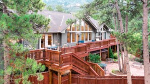 Une maison à deux étages avec une terrasse, entourée de pins.