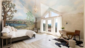Une chambre à coucher avec un grand lit, un bureau, une chaise, une lampe et une vue sur un paysage montagneux par la fenêtre.