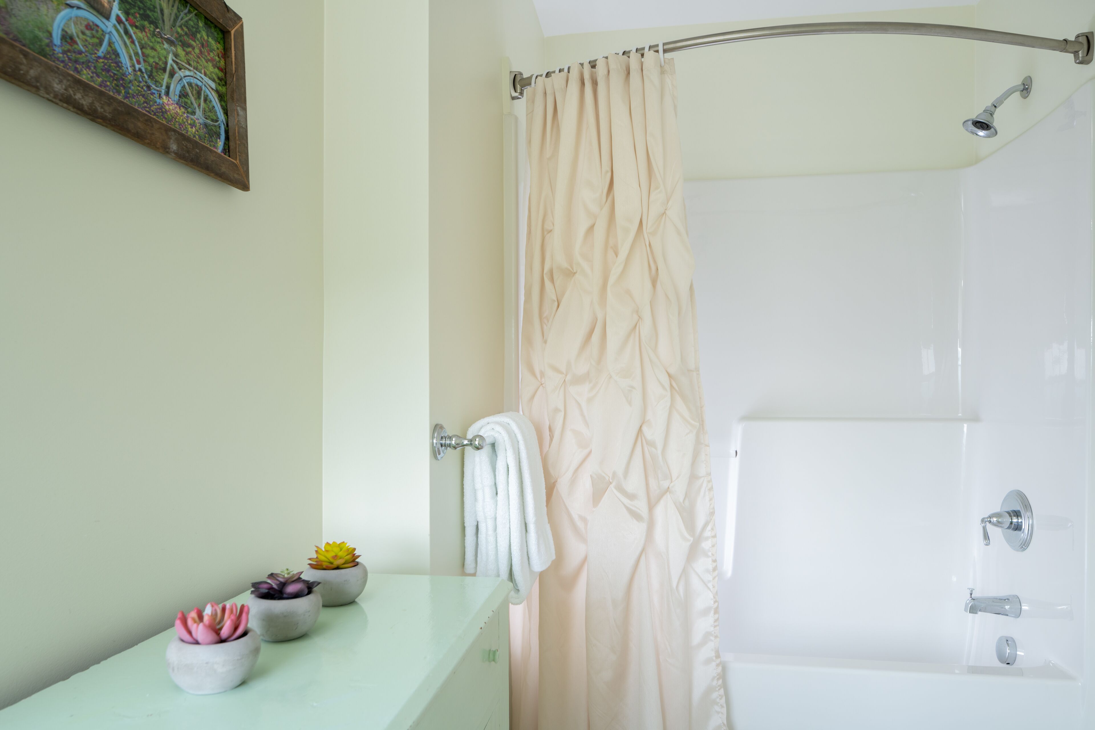 A bathroom with a bathtub, a shower curtain, a towel rack, and three potted plants on the counter.