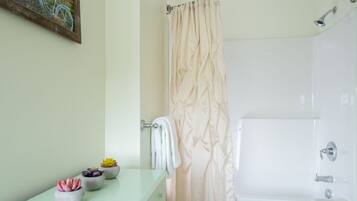 A bathroom with a bathtub, a shower curtain, a towel rack, and three potted plants on the counter.