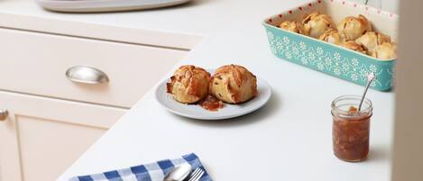 Una encimera de cocina con un plato de manzanas, un bol de pasteles y un frasco de mermelada.