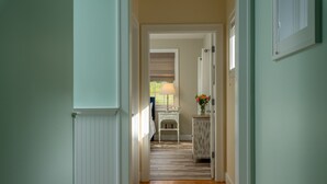 Un couloir doté d’un plancher en bois, d’un banc blanc, d’une lampe et d’un vase rempli de fleurs.