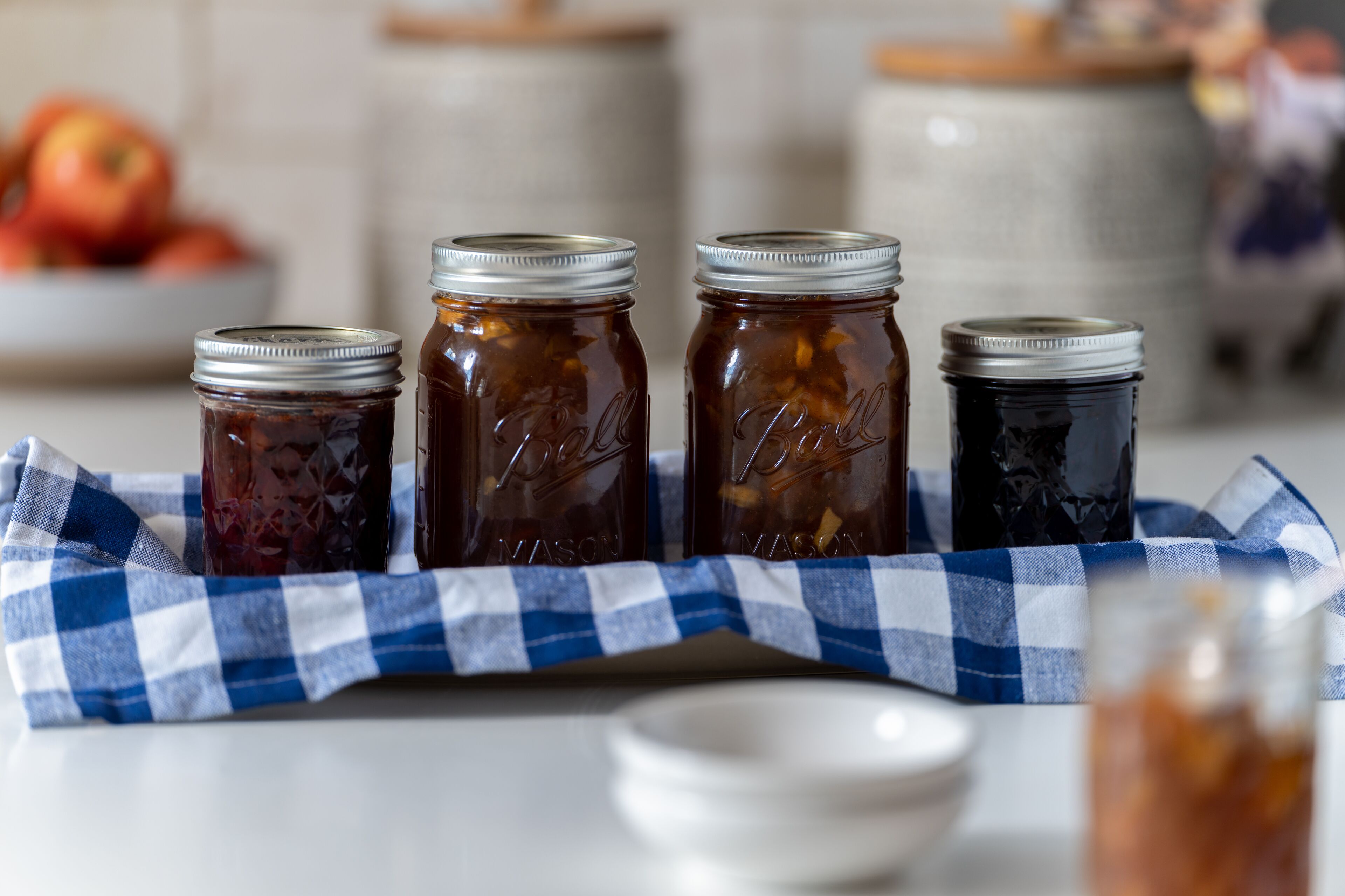 Four glass jars with metal lids on a blue and white checkered cloth.